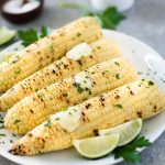 close up front view of grilled corn on the cob with butter and lime wedges