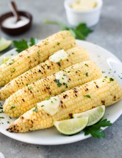 close up front view of grilled corn on the cob with butter and lime wedges