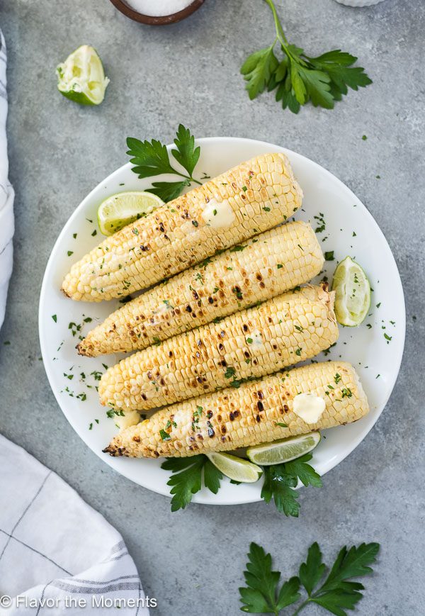 overhead shot of grilled corn on the cob on a white plate with melted butter on top