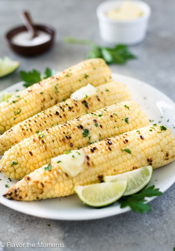 front view of grilled corn on the cob on a white plate with melting butter on top