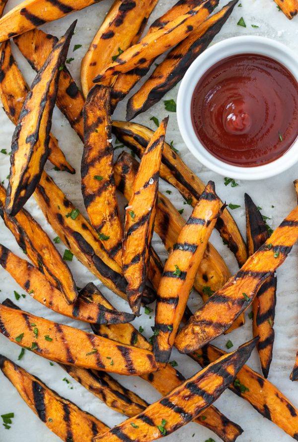 closeup view of grilled sweet potato fries on parchment with ketchup