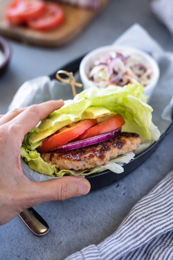 Hand holding grilled turkey burgers in a lettuce wrap