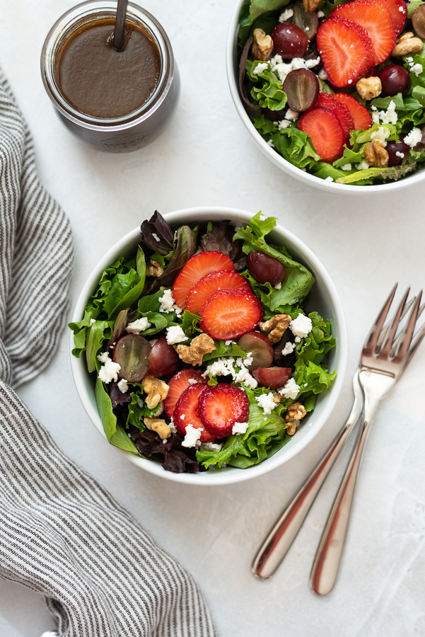 Strawberry salad in white bowl with two forks and linen alongside