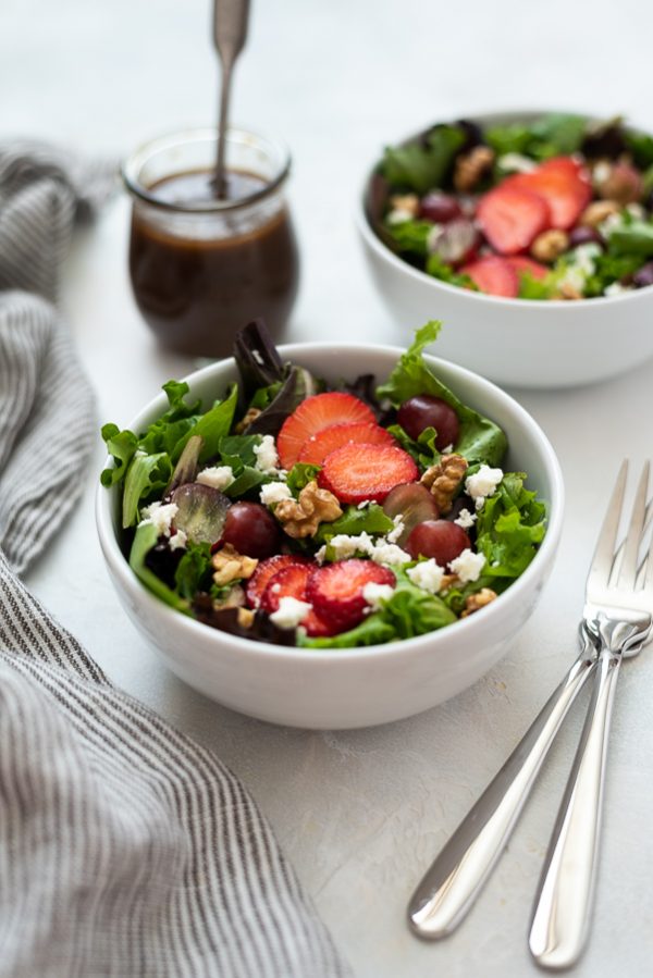 front view of strawberry salad in white bowl with dressing in background