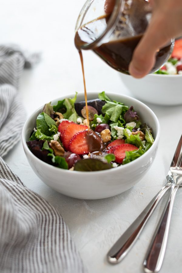 strawberry salad in white bowl with balsamic dressing drizzling