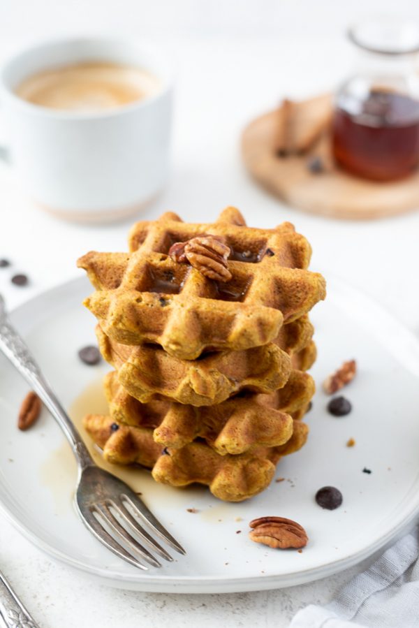 Stack of pumpkin oat flour waffles with pecans and maple syrup