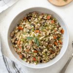 overhead shot of low carb riced cauliflower stuffing in serving bowl with sage on top