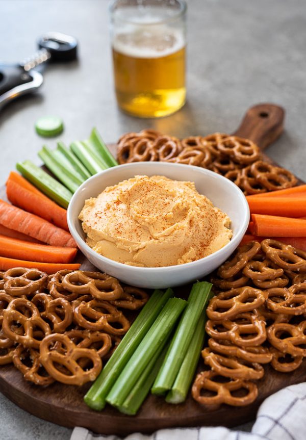 wooden server with bowl of pub cheese and pretzels, carrots and celery