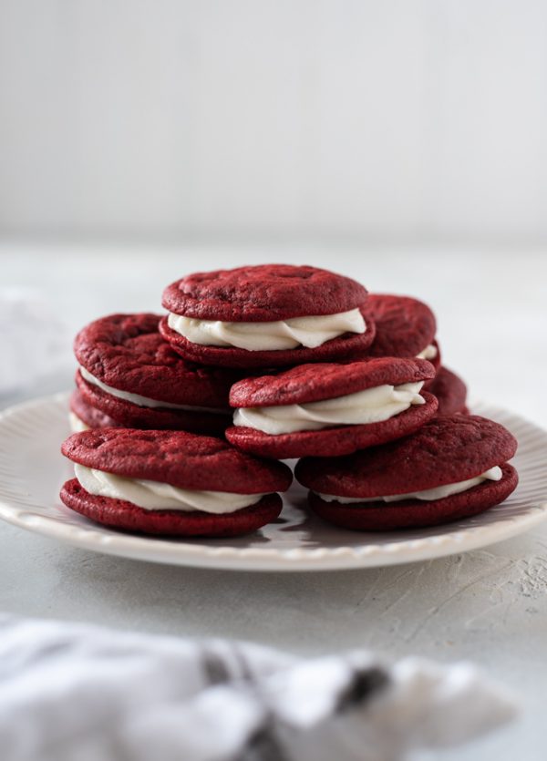 Red velvet sandwich cookies piled high on a white plate