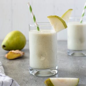 Pear smoothie in glass with striped straw and slice of pear
