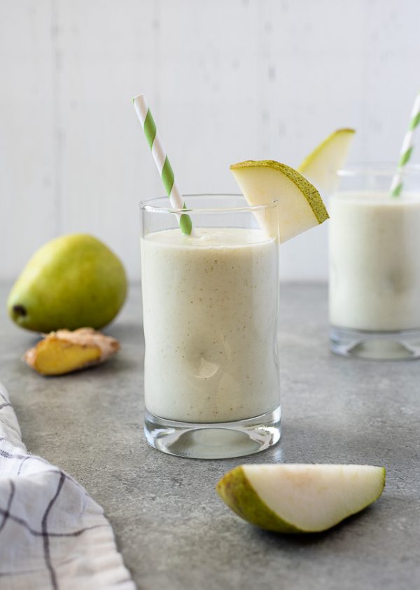 pear smoothie with slice of pear on the top of the glass and green striped straw