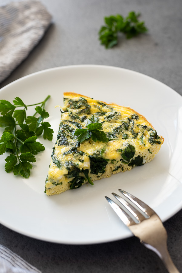 slice of spinach feta frittata on white plate with parsley