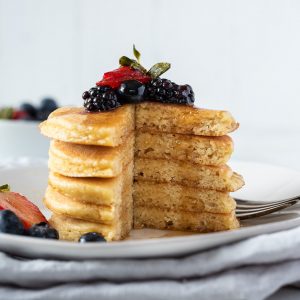 stack of almond flour pancakes with berries on top and maple syrup dripping