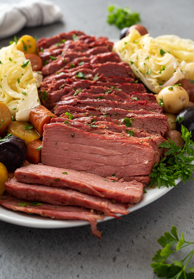 angled front shot of sliced corned beef and cabbage on a white serving platter