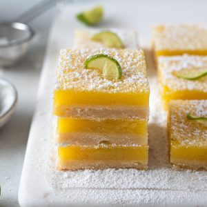 key lime bars stacked up on a white serving board with powdered sugar