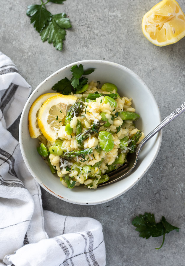 spring risotto in a bowl with fork with lemon and oarsley