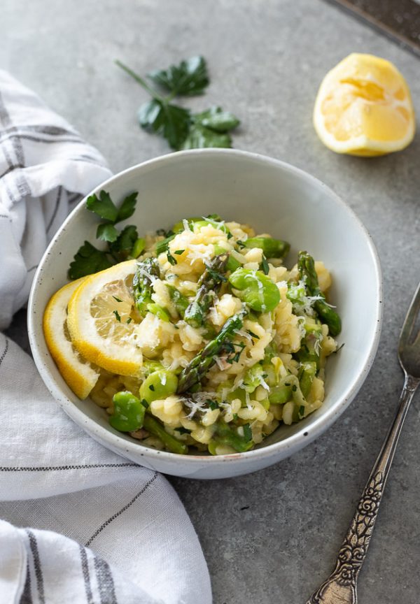 spring vegetable risotto in bowl topped with lemon, parsley and parmesan