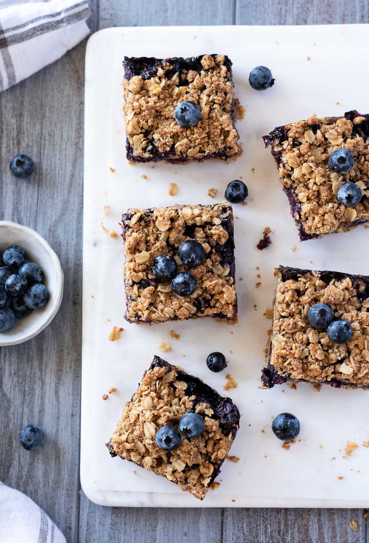 Blueberry crumble bars on a marble board with blueberries