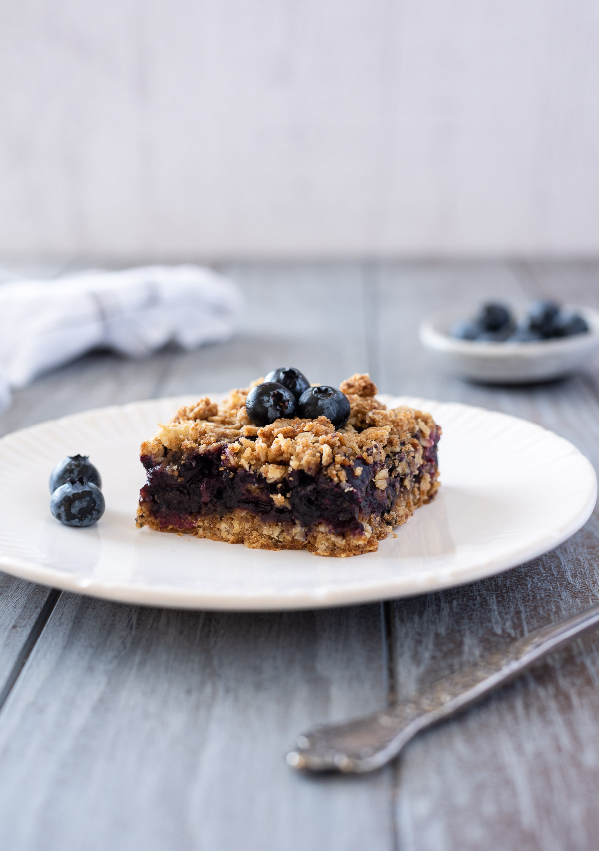 Blueberry crumble bar on a white plate with blueberries