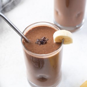 close up of chocolate banana protein smoothie with metal straw and banana on rim