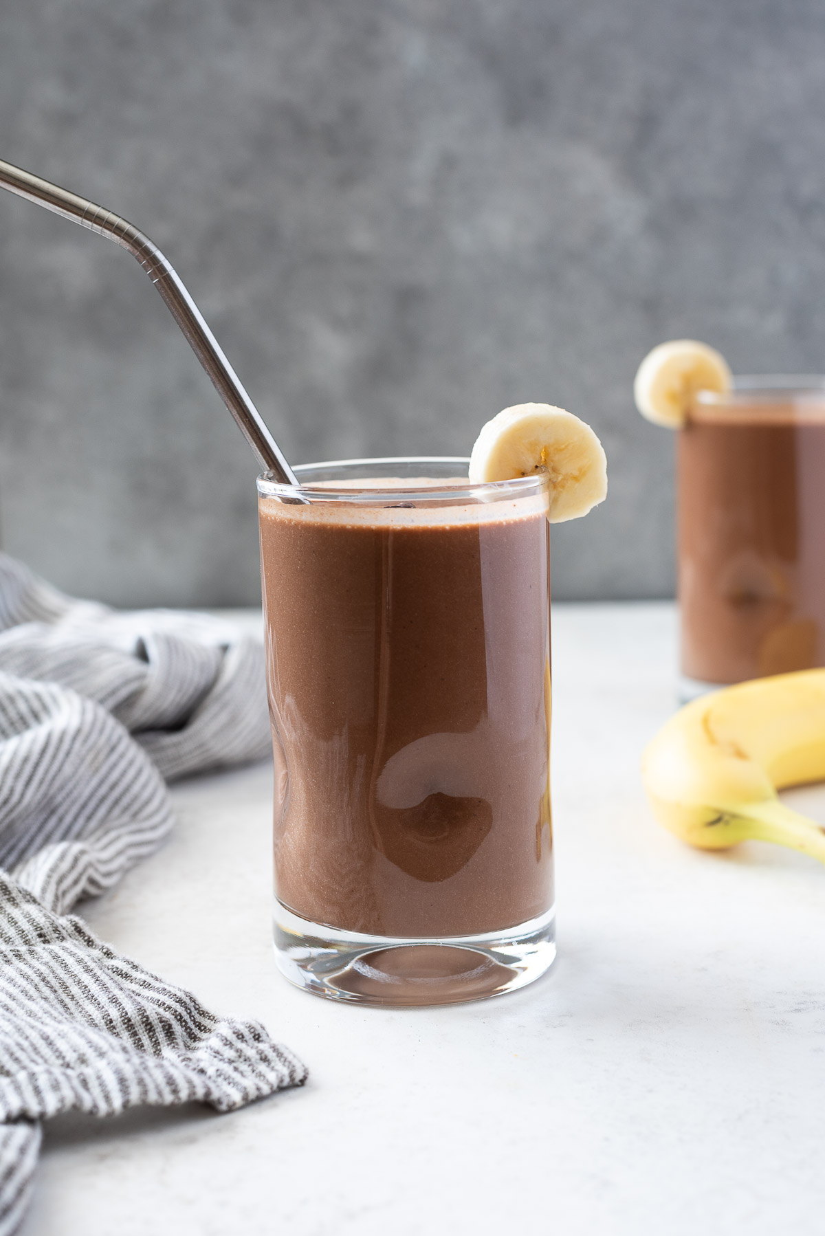 chocolate protein smoothie in a glass with banana slice on the rim
