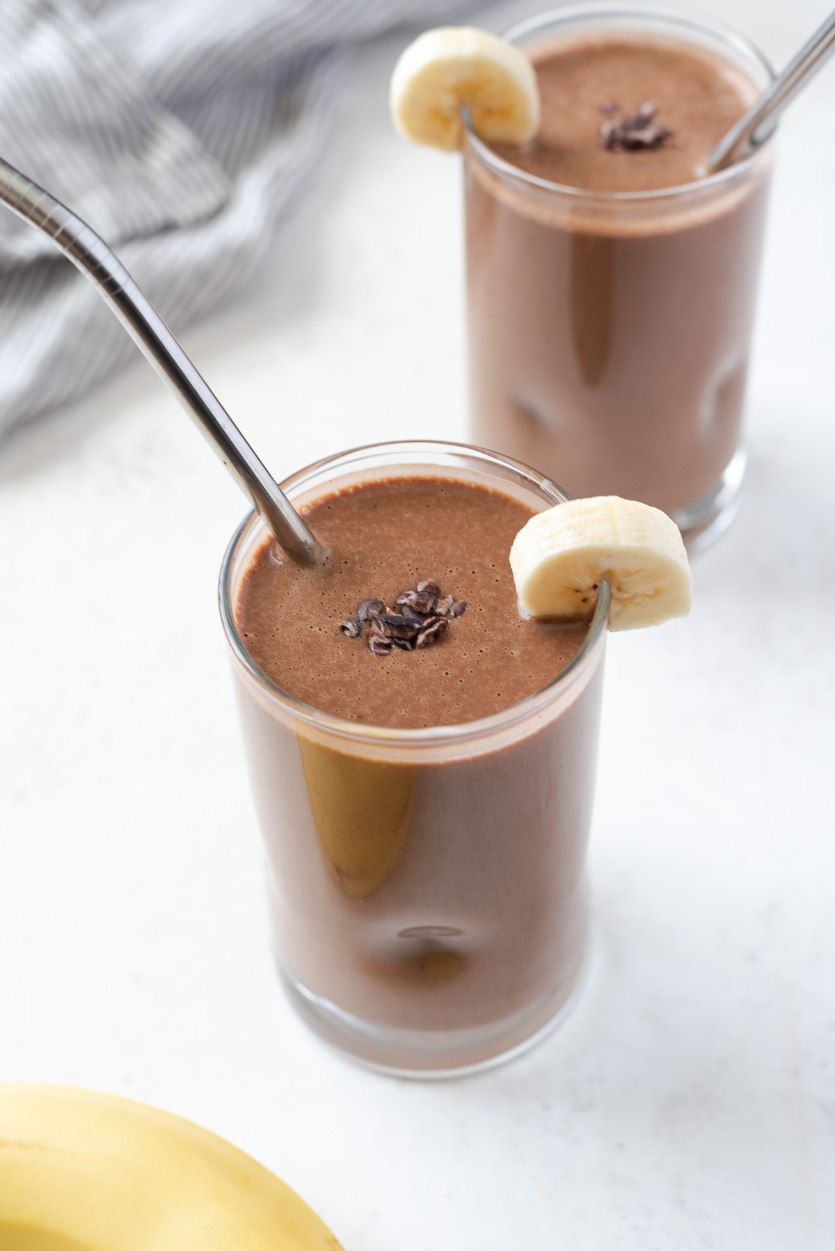 glass of chocolate banana protein smoothie with cacao nibs and banana on top