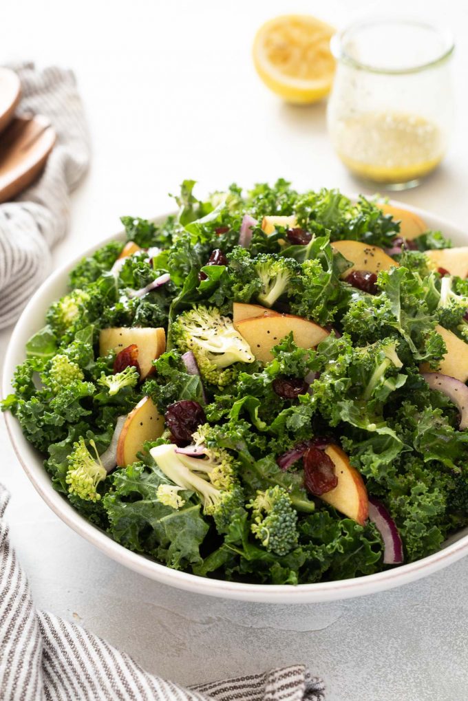 Broccoli kale salad in white bowl with lemon poppy seed dressing behind