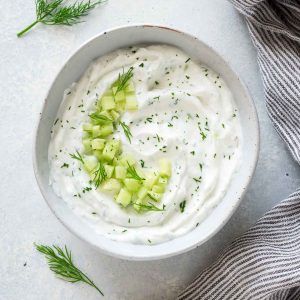 Greek tzatziki sauce in white bowl with cucumber and dill on top