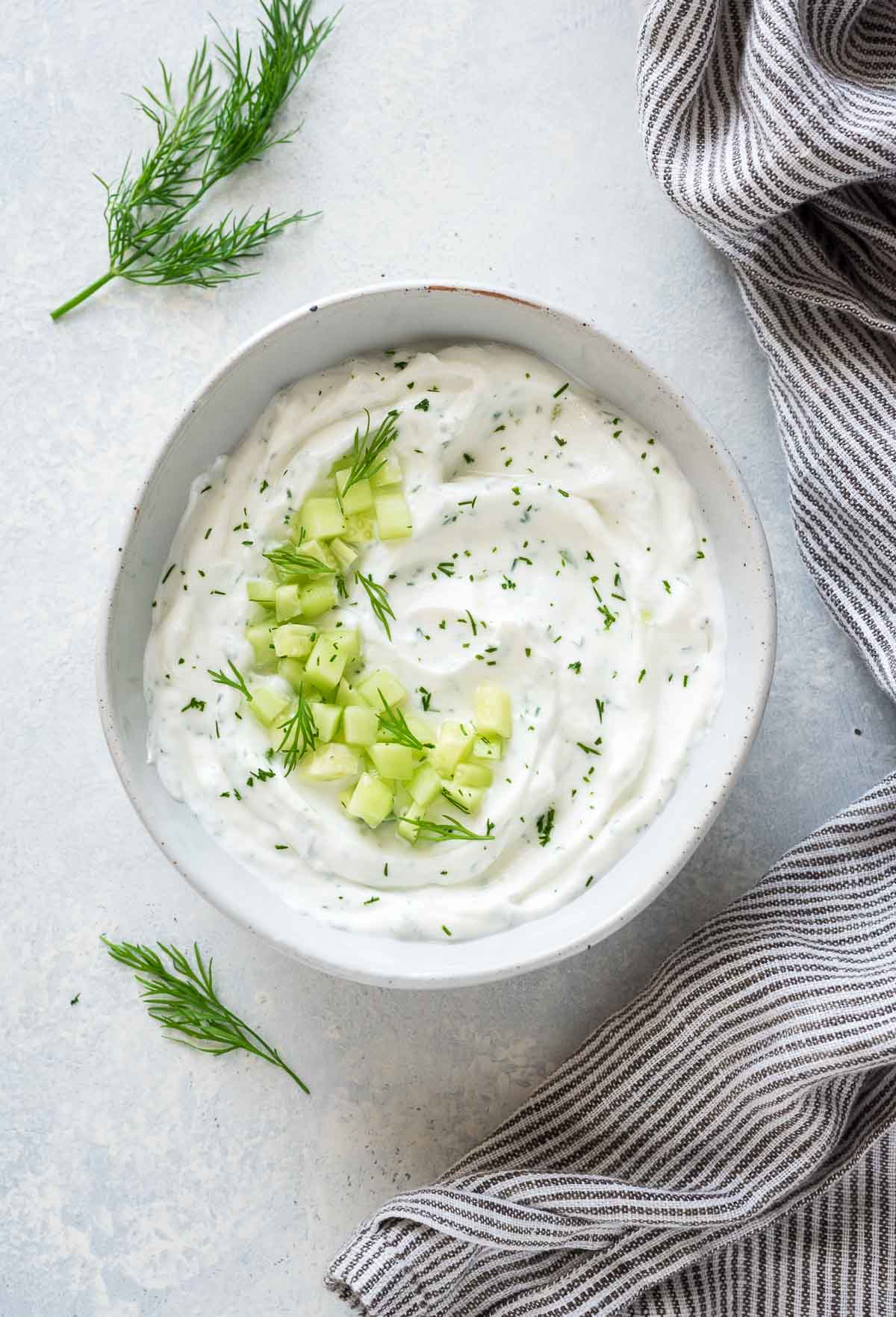 Close up of Greek tzatziki sauce in white bowl with cucumber and dill on top