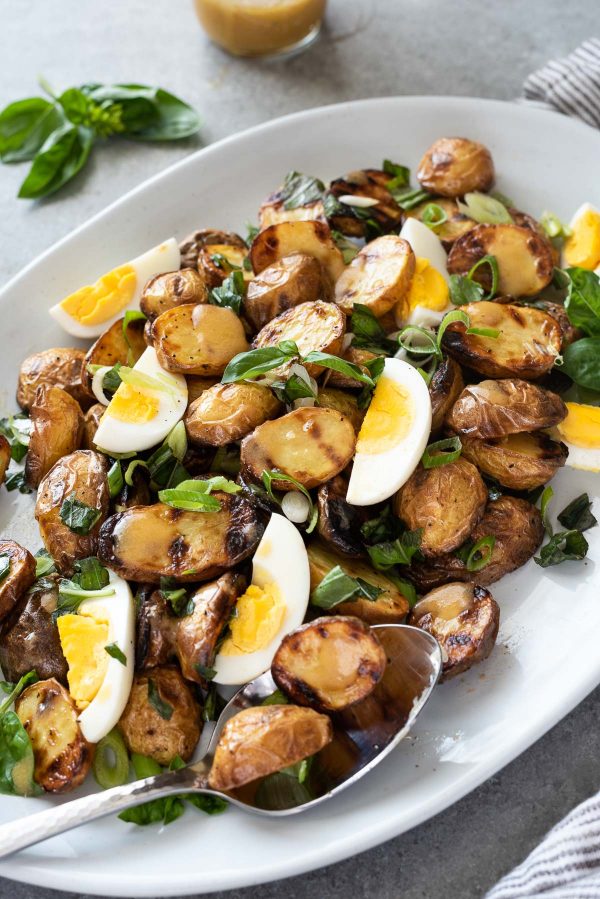 Close up of grilled potato salad on platter with spoon and basil