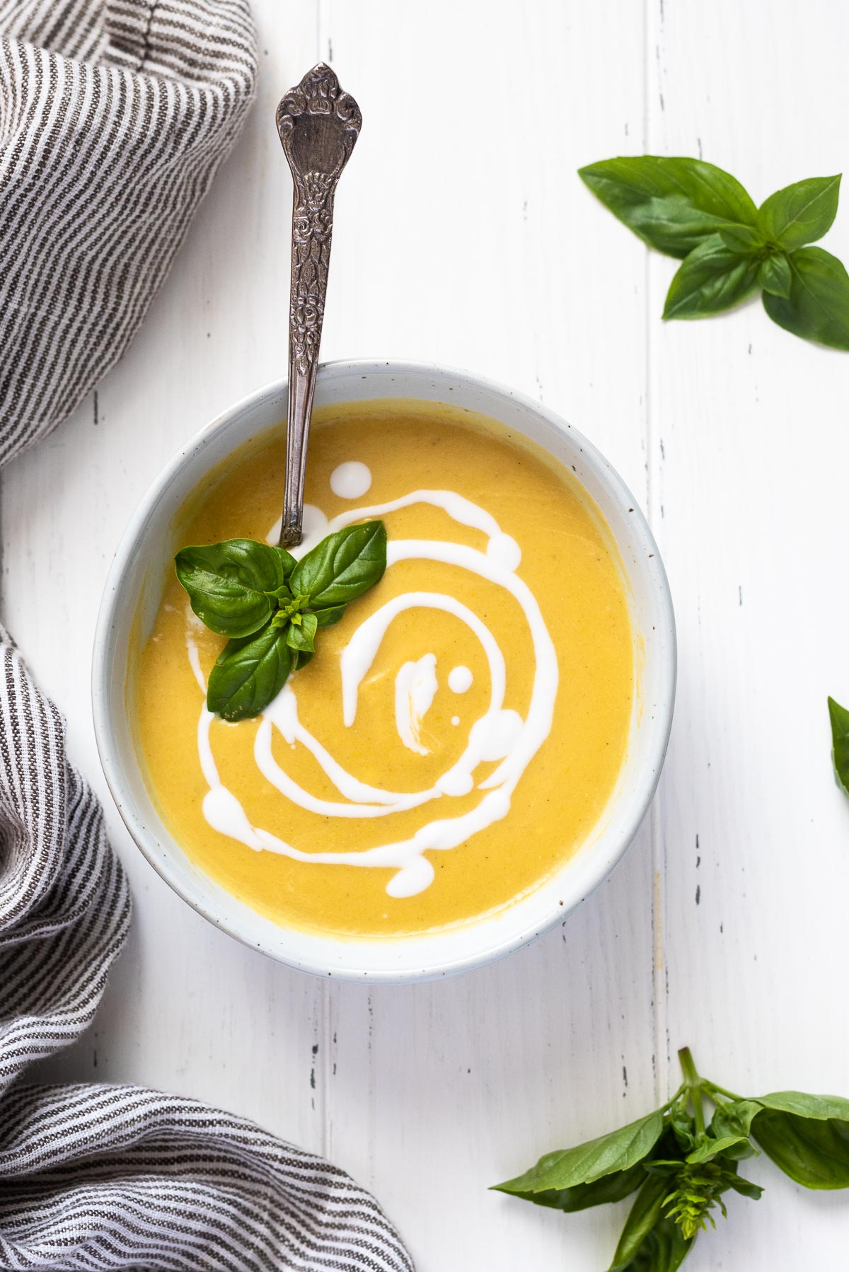 Summer squash soup in white bowl with coconut milk and basil on top