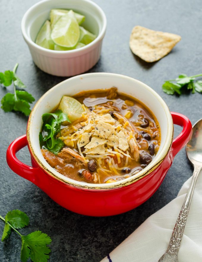 Chicken tortilla soup in a red bowl with chips and cilantro