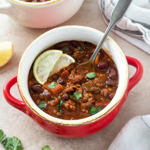 Chorizo chili in a red bowl with lime and cilantro