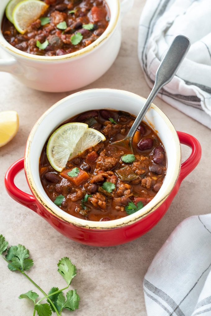 Chorizo chili in a red bowl with lime and cilantro