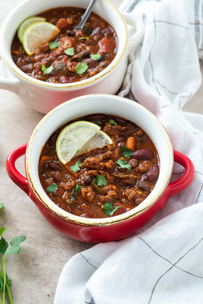 Spicy chorizo chili in a red bowl with lime slices on top