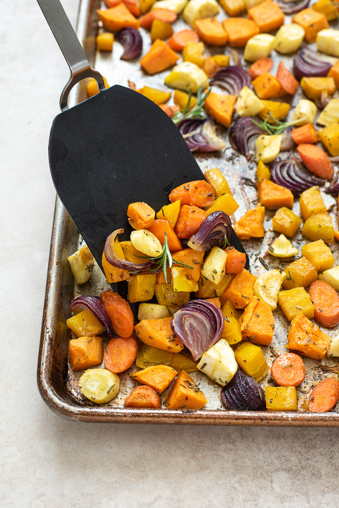 Spatula scraping off roasted root vegetables on a sheet pan