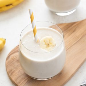 Banana smoothie in a glass with straw and banana slice