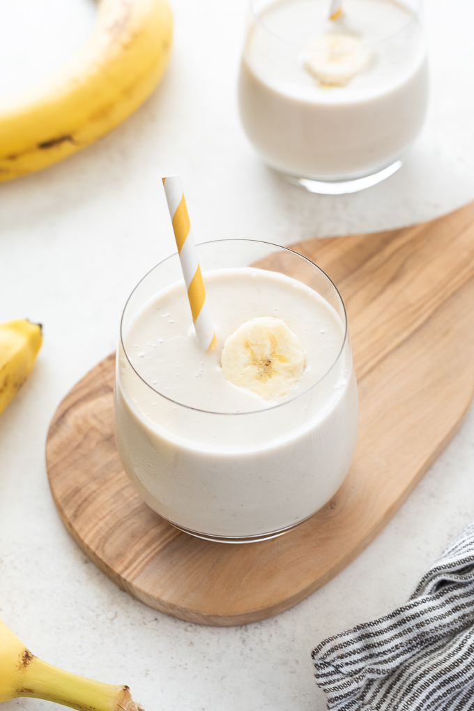 Glass of banana smoothie on small wooden cutting board