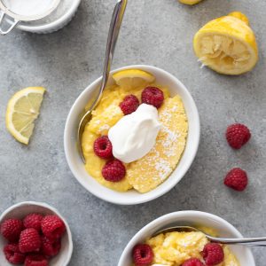Lemon pudding cake in bowls with raspberries and whipped cream