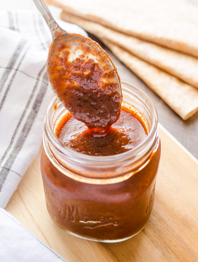 Red enchilada sauce dripping off a spoon into a jar