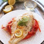 Baked catfish topped with fennel fronds on a white plate.