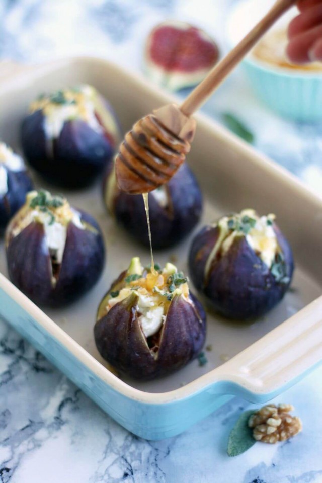 Figs stuffed with goat cheese being drizzled with honey. The figs are in a blue baking dish.