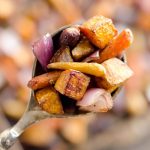 A spoonful of roasted root vegetables being held aloft.