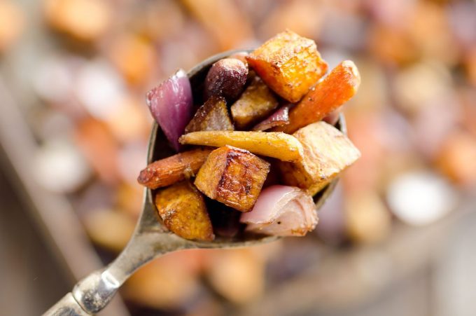 A spoonful of roasted root vegetables being held aloft.