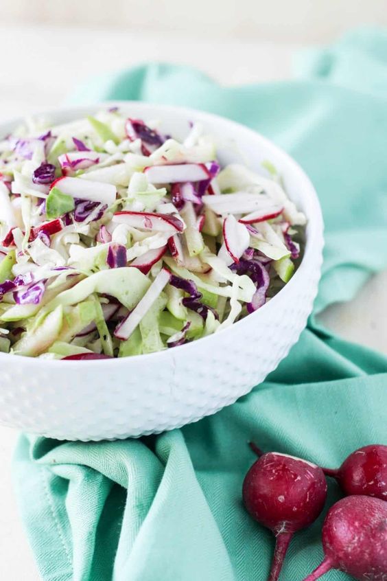 A white bowl of cabbage, radish, and apple coleslaw on a blue towel.