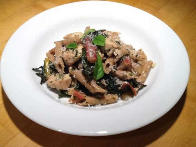 A white plate of chicken pasta with chard.