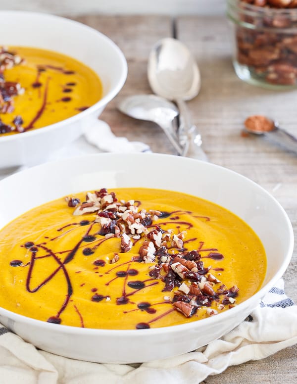 Two bowls of kabocha squash soup topped with pecans and a cherry drizzle.