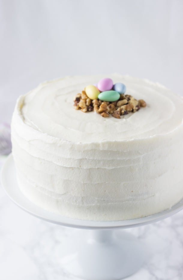 A frosted carrot cake on a white cake stand.