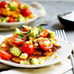 A corn cake topped with tomatoes, avocado and fresh corn.