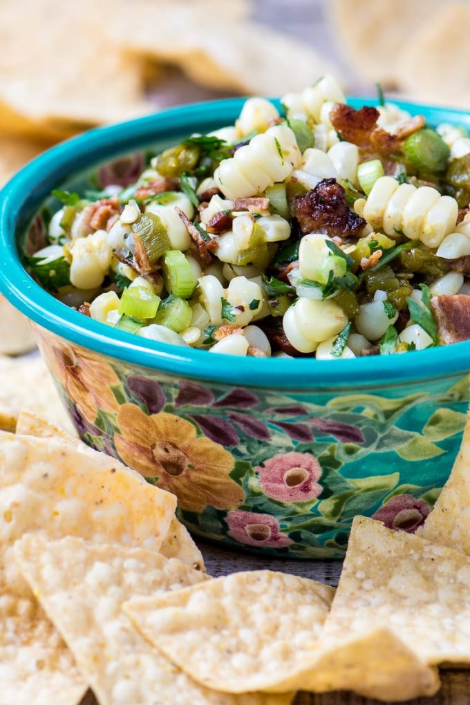 A floral bowl of corn and bacon salsa surrounded by tortilla chips.